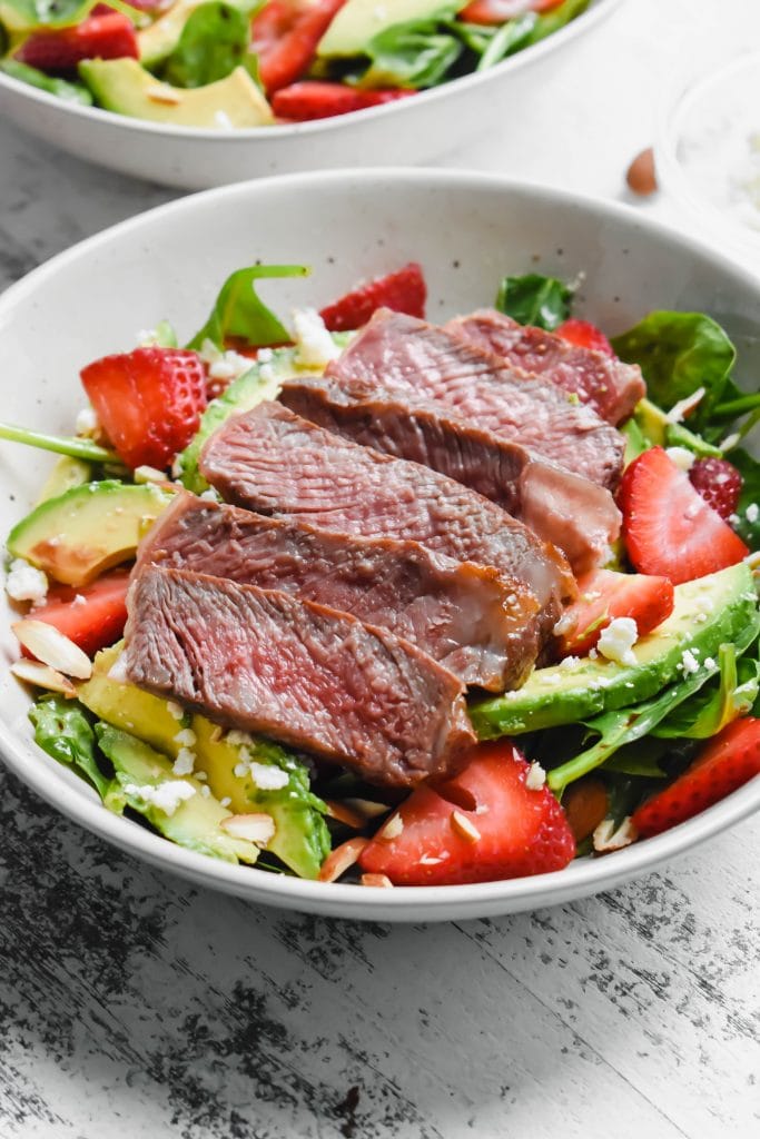 spinach salad with strawberries, avocado and steak in a white bowl
