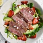 spinach salad with strawberries, avocado and steak in a white bowl