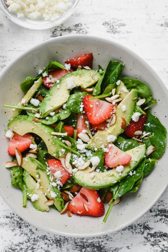 spinach salad with strawberries, avocado in a white bowl