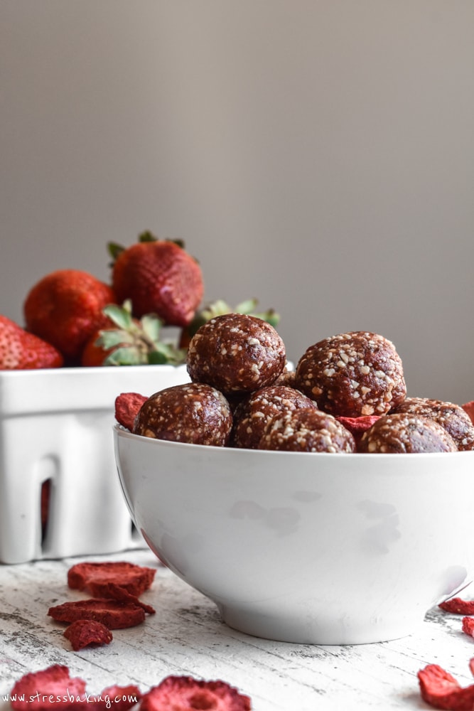 Strawberry Cashew Energy Bites in a bowl with freeze dried strawberries and fresh strawberries in the background