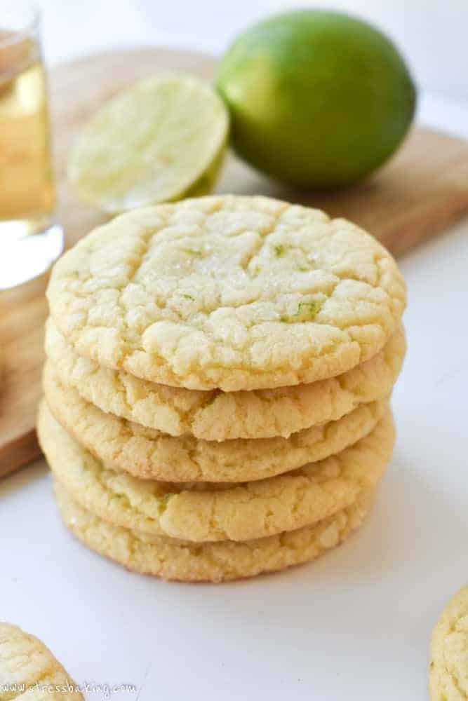 Chewy margarita cookies stacked on a white surface with limes and tequila