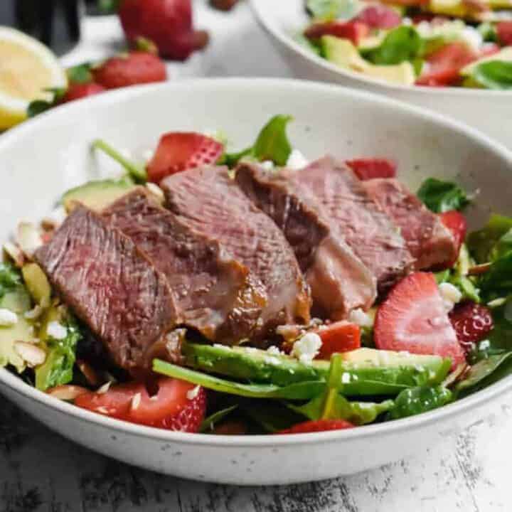 spinach salad with strawberries, avocado and steak in white bowls