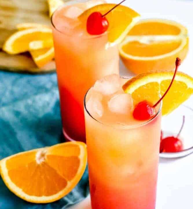 Tequila sunrise cocktails on a white surface with a teal napkin and orange slices
