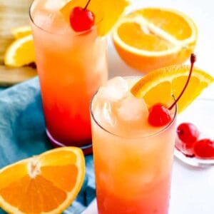 Tequila sunrise cocktails on a white surface with a teal napkin and orange slices