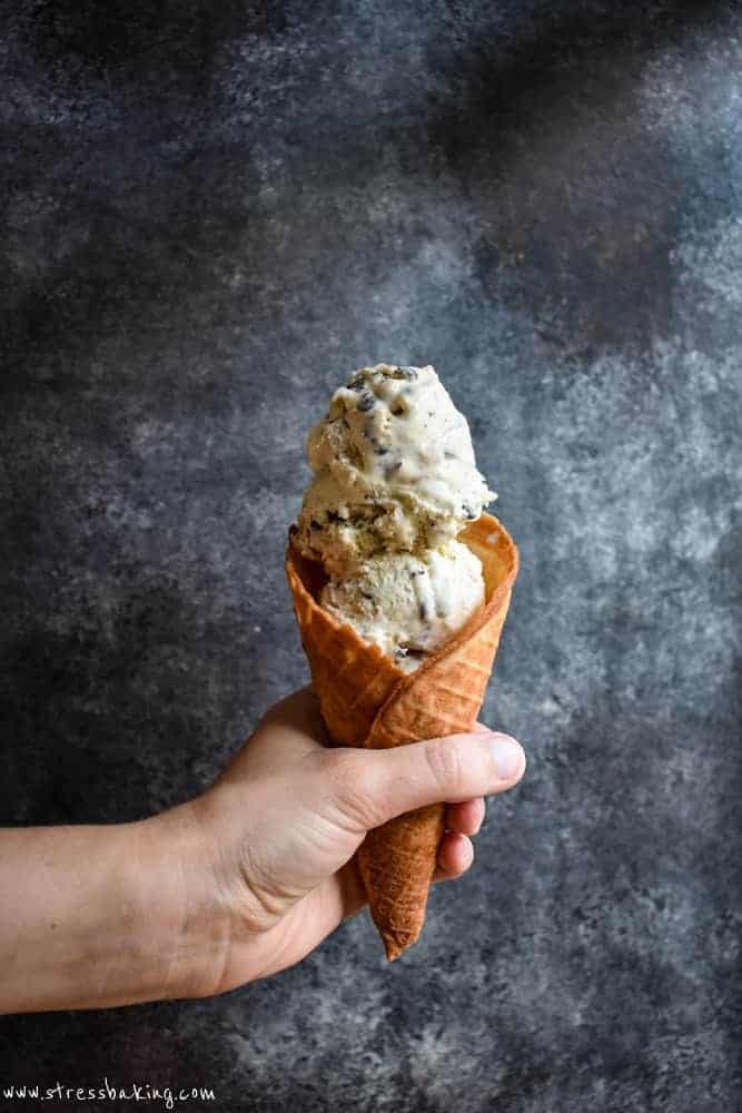 Chocolate chip cookie dough in a waffle cone being held in front of a dark background