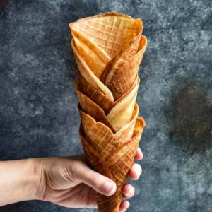 Waffle cones stacked and being held against a dark background