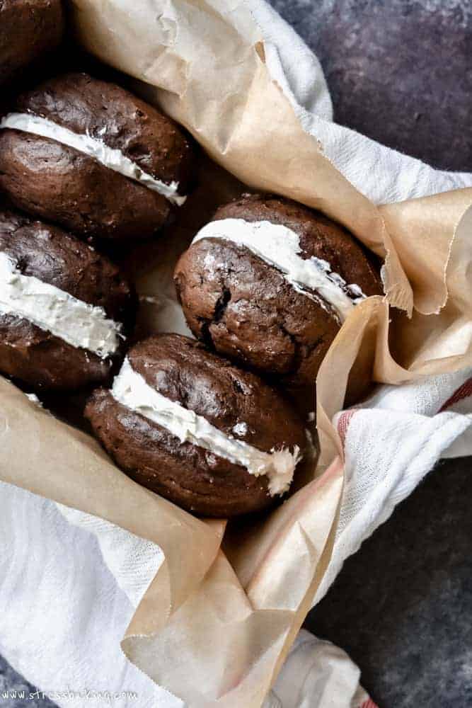 Chocolate whoopie pies stored on their sides in a loaf pan lined with a tea towel and parchment paper