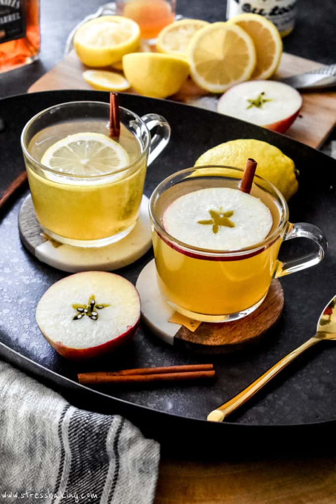 Two hot toddies in clear mugs topped with fruit garnishes