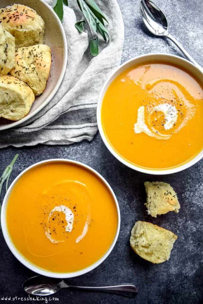 Overshot shot of two bowls of vibrant orange butternut squash soup in white bowls with swirls of coconut milk