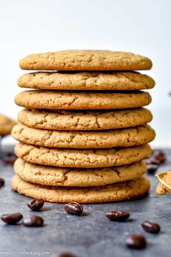 Side shot of a stack of peanut butter espresso cookies on a baking sheet surrounded by espresso beans