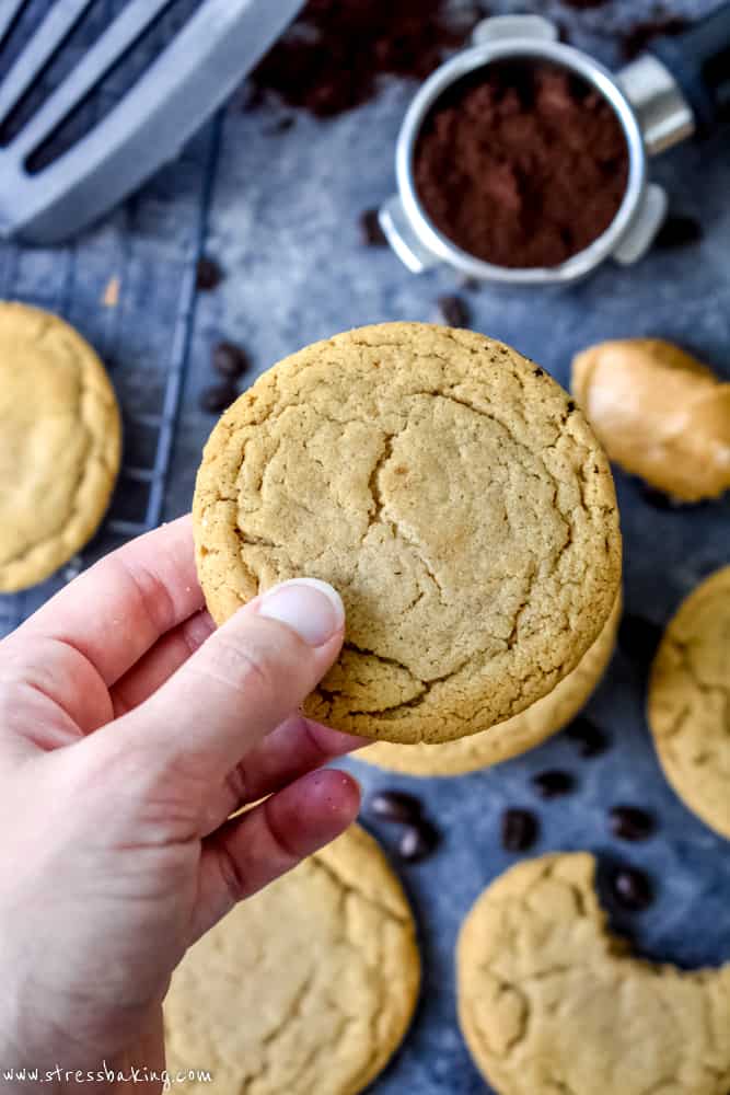 Hand holding a crinkly peanut butter espresso cookie above a baking sheet
