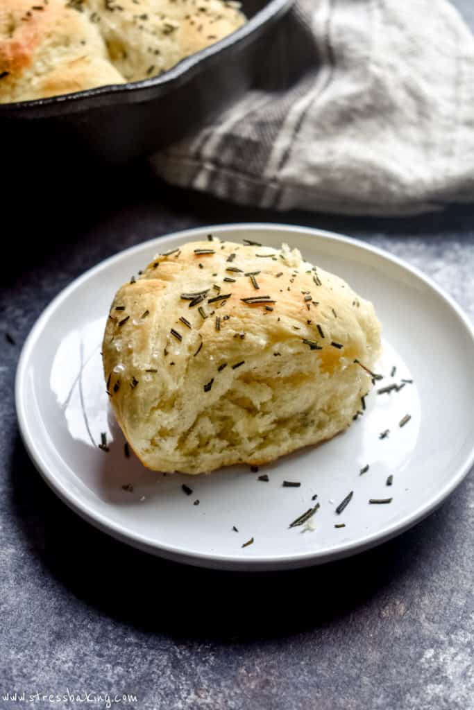 Golden dinner roll on a white plate topped with chopped rosemary