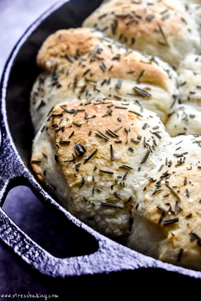 Close up of dinner rolls in a black skillet topped with rosemary
