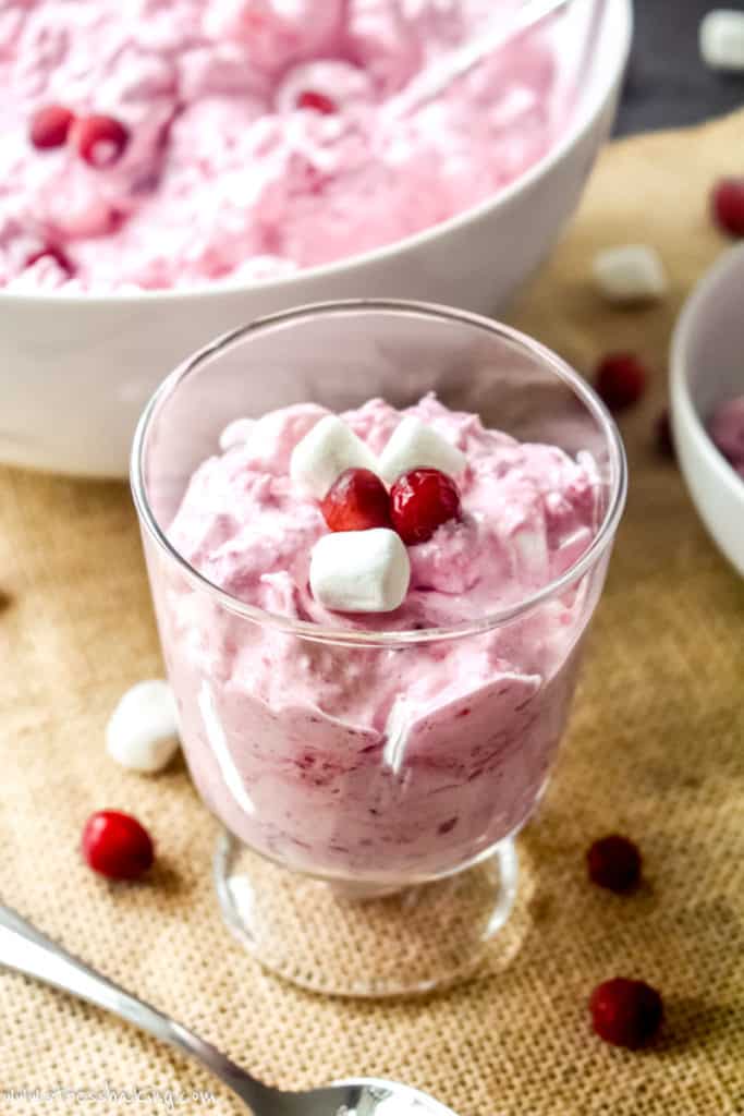 Vibrant pink cranberry fluff in a trifle dish topped with mini marshmallows and cranberries