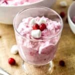Vibrant pink cranberry fluff in a trifle dish topped with mini marshmallows and cranberries