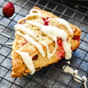 A vibrant cranberry scone on a black wire rack topped with a large drizzle of white vanilla icing