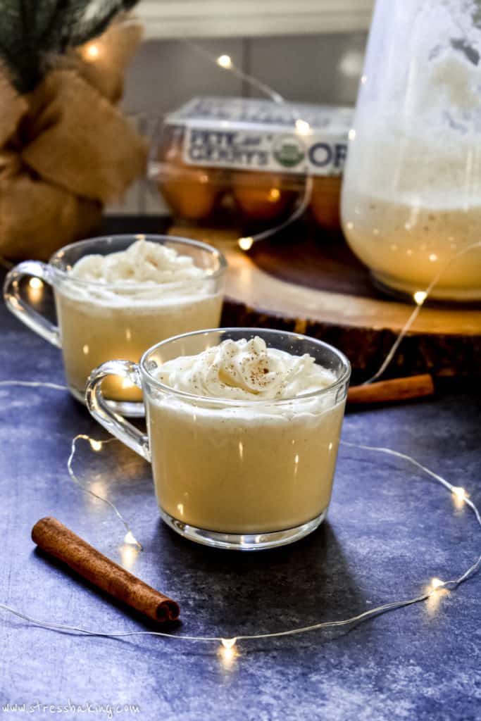 Two clear mugs filled with creamy homemade eggnog and topped with whipped cream and nutmeg