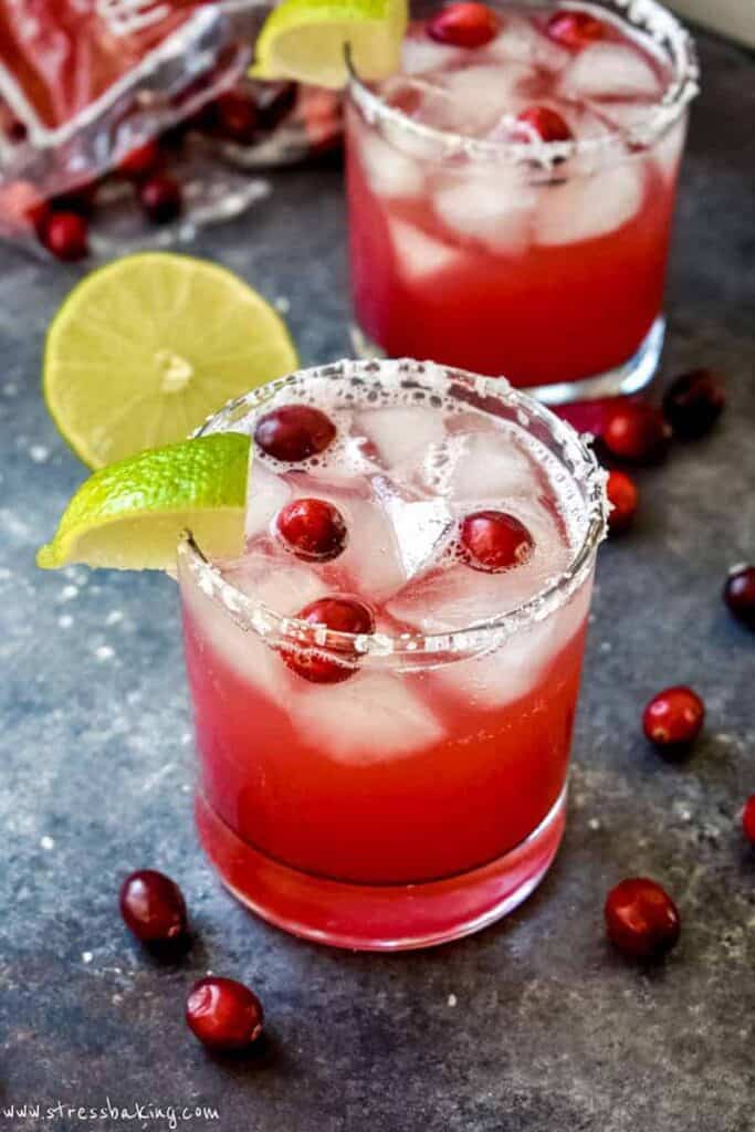 A vibrant red cranberry champagne margarita in a clear glass garnished with fresh cranberries and a lime wedge