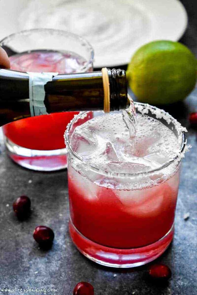 Champagne being poured into a glass of cranberry champagne margarita