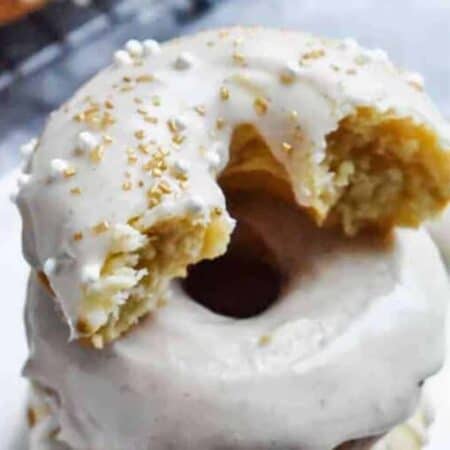 A stack of eggnog donuts with a bite taken out of the one on top