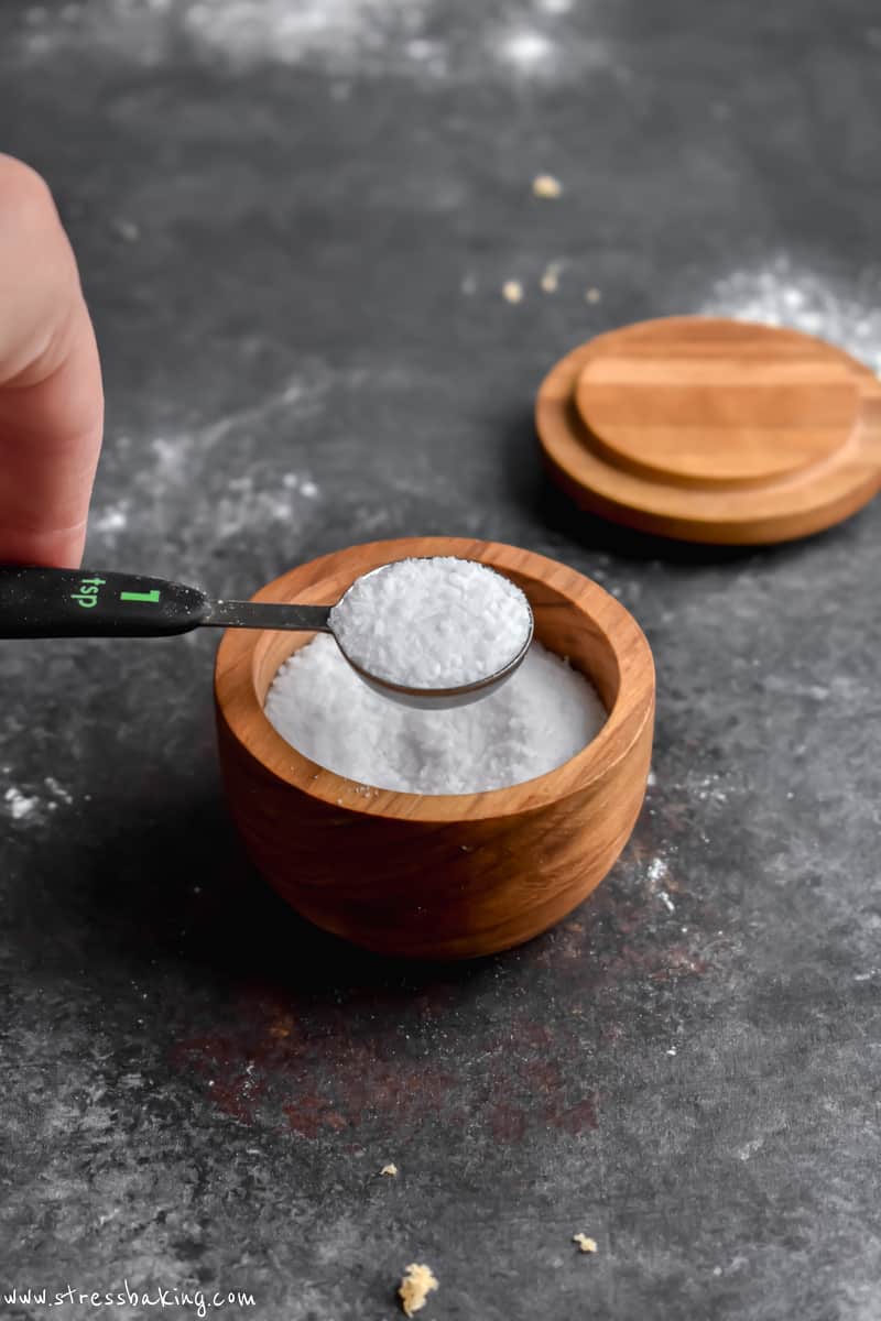 A measuring spoon holding salt over a salt cellar
