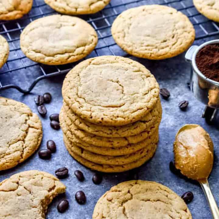 Crinkly peanut butter espresso cookies on a baking sheet with espresso beans and a spoon of peanut butter