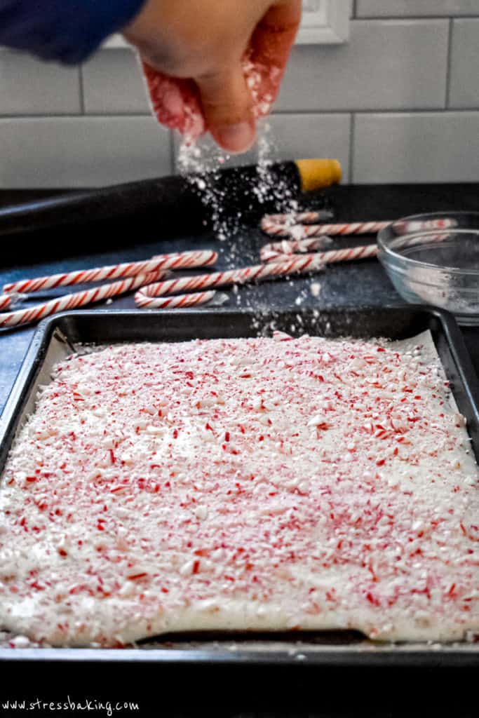 Hand sprinkling crushed peppermint on top of a pan of white chocolate