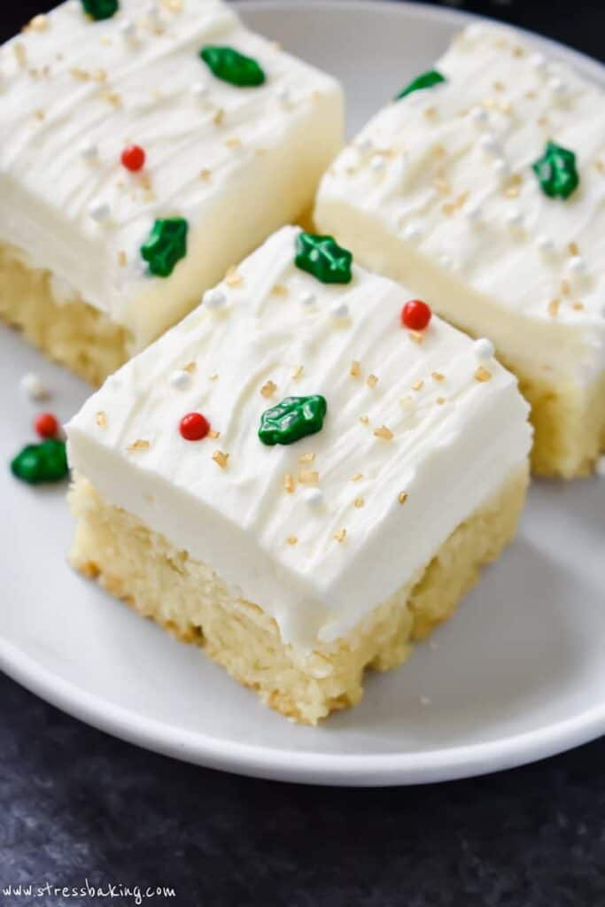 A sugar cookie bar on a white plate decorated with white frosting and festive sprinkles