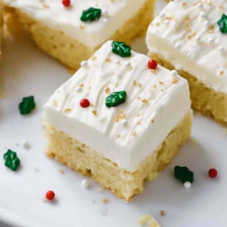Sugar cookie bars on a white plate decorated with white frosting and festive sprinkles