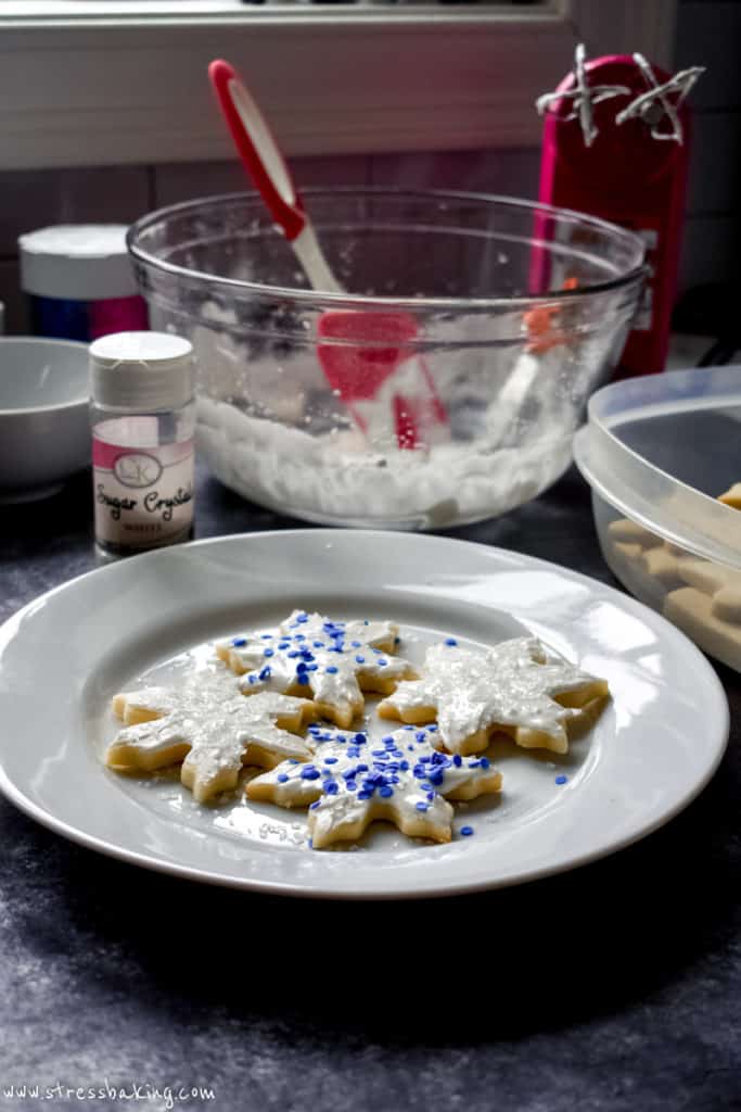 A plate of decorated snowflake sugar cookies on a table of baking supplies