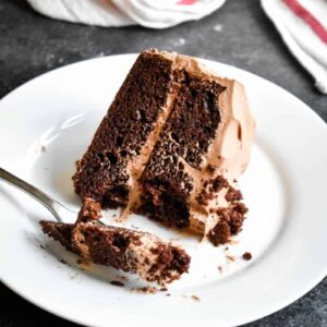 A slice of two layer chocolate cake on a white plate with a fork and a bite taken out