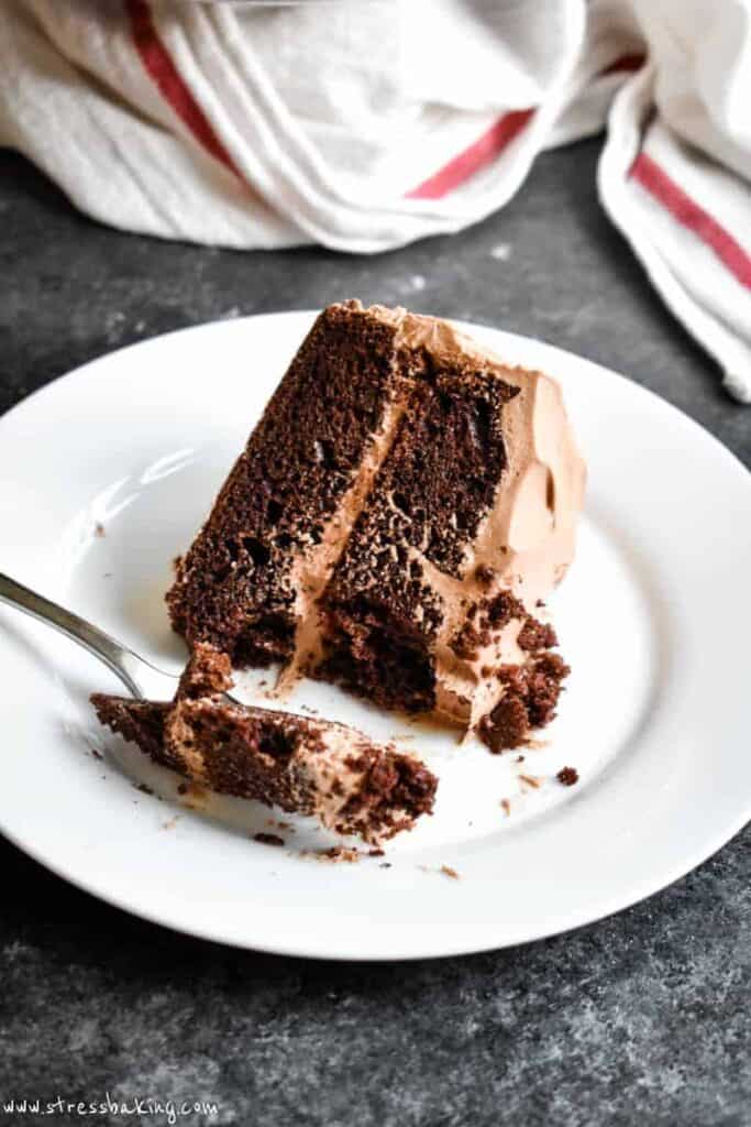 A slice of two layer chocolate cake on a white plate with a fork and a bite taken out