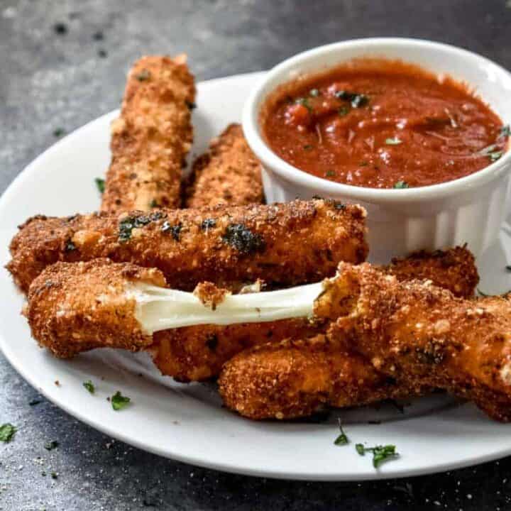 A plate of golden brown mozzarella sticks with one pulled apart to show the melted cheese