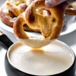 A golden brown soft pretzel being dipped in cheese