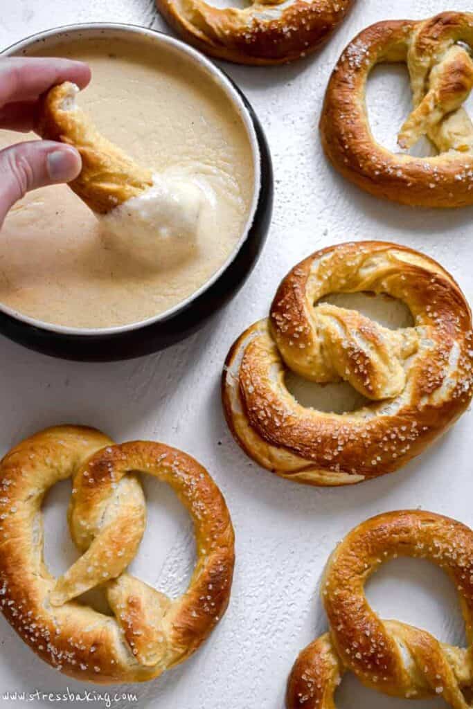 Golden brown soft pretzels on a white counter with one being dipped in cheese