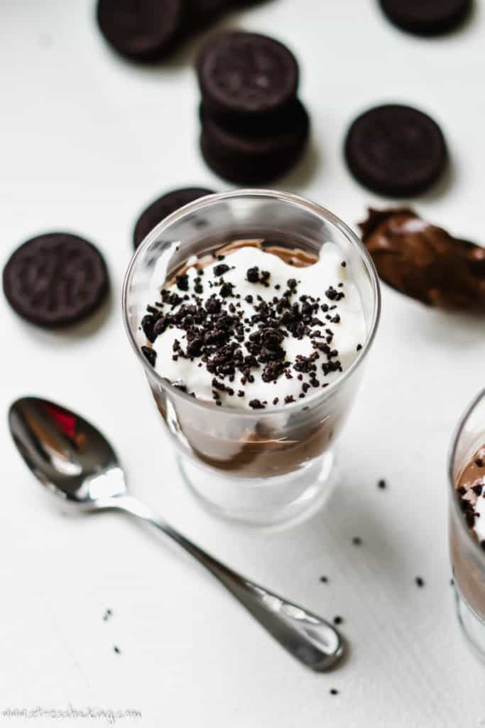 A trifle dish with layers of Nutella mousse, whipped cream and topped with crushed Oreos with a spoon