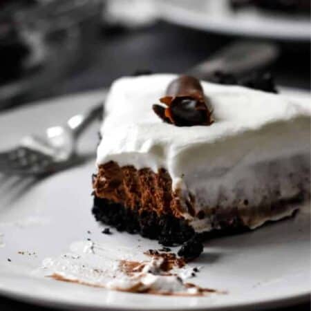 A slice of Bailey's chocolate pie topped with whipped cream and chocolate shavings with a fork on a white plate