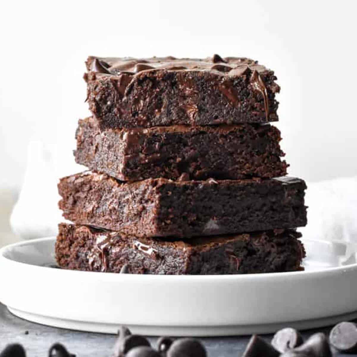 A stack of fudgy brownies with pockets of melted chocolate on a white plate