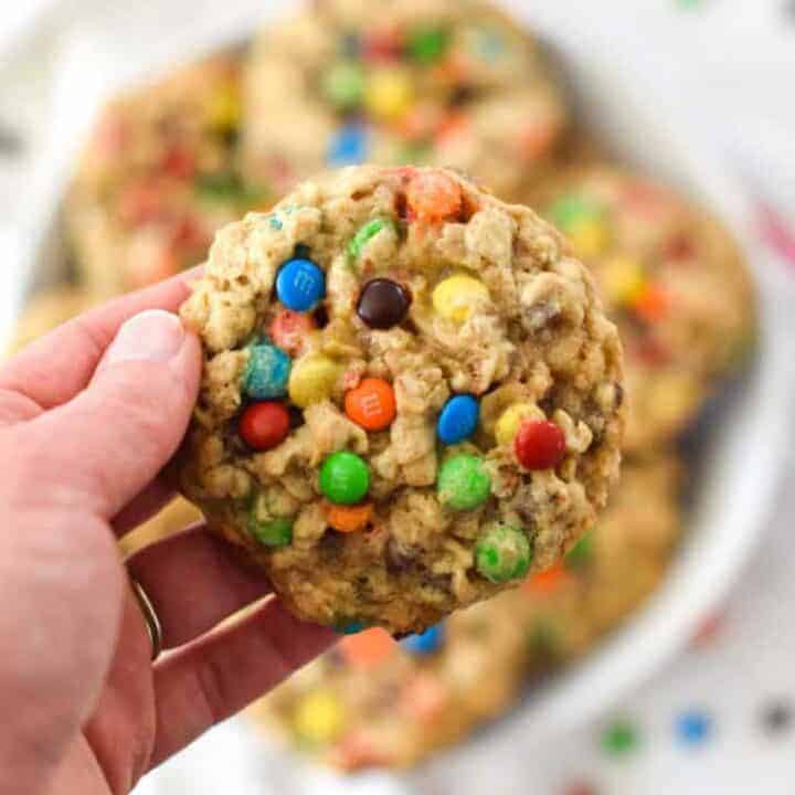 Overhead shot of a colorful oatmeal M&M cookie being held over a plate of cookies