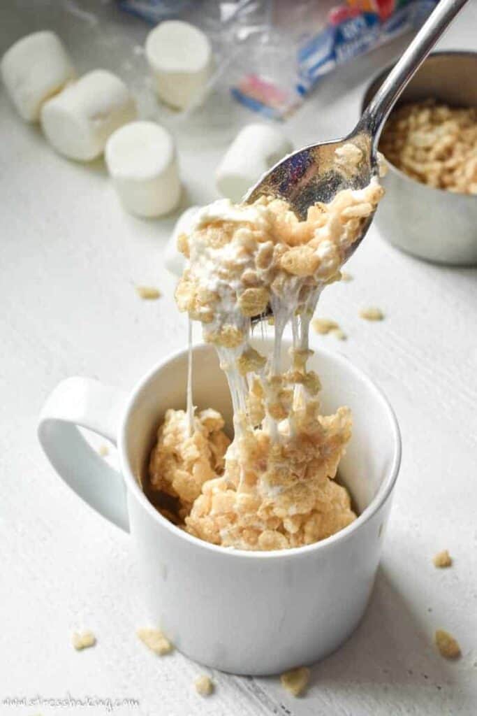 A spoonful of Rice Krispie treat in a white mug being pulled out to show the melty marshmallow