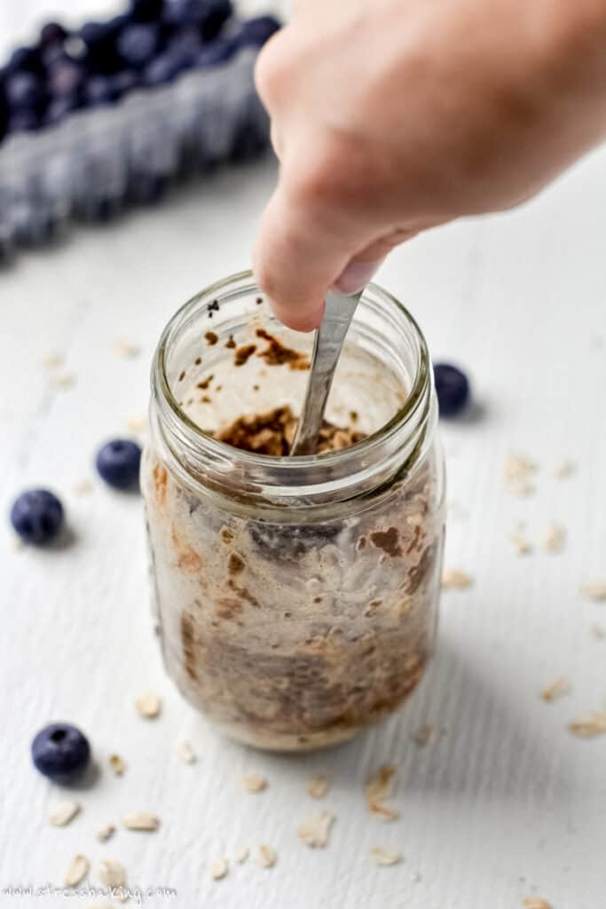 A hand stirring the ingredients inside a mason jar with a spoon