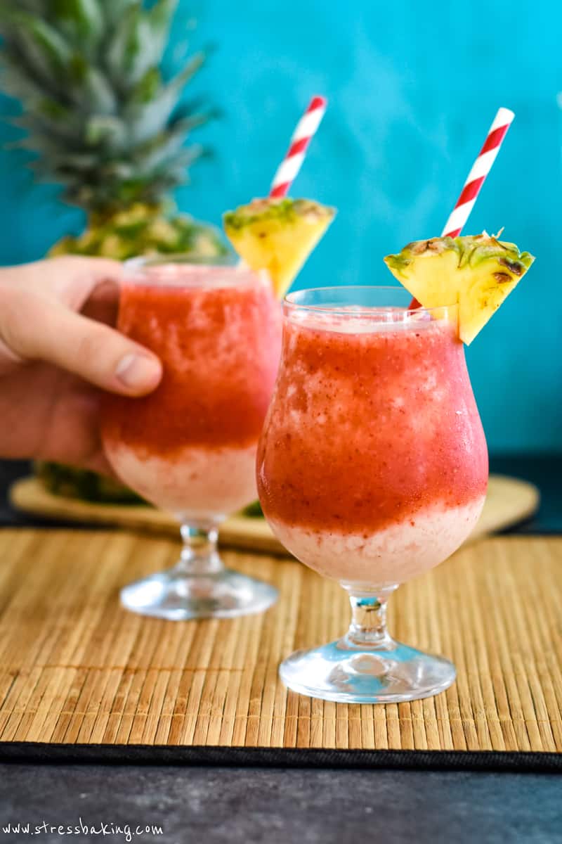 Two vibrant red and cream colored frozen drinks with wedges of pineapple