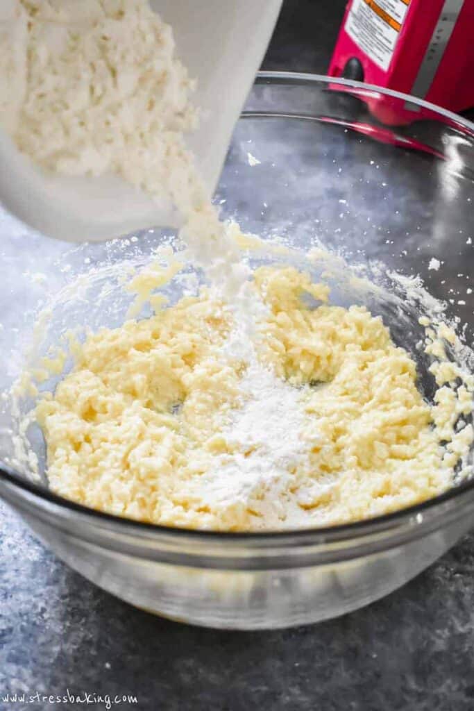 Flour mixture being poured into a bowl of creamed butter and sugar