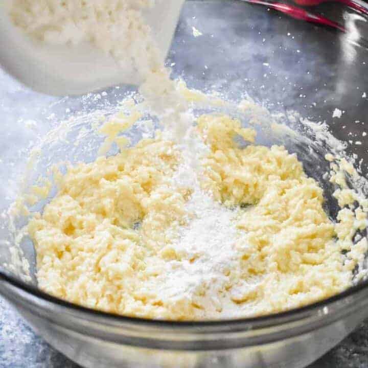 Flour mixture being poured into a bowl of creamed butter and sugar