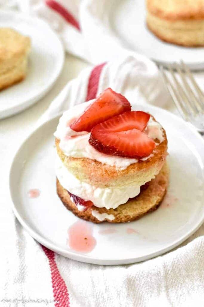 Homemade strawberry shortcake on a white plate topped with sliced strawberries