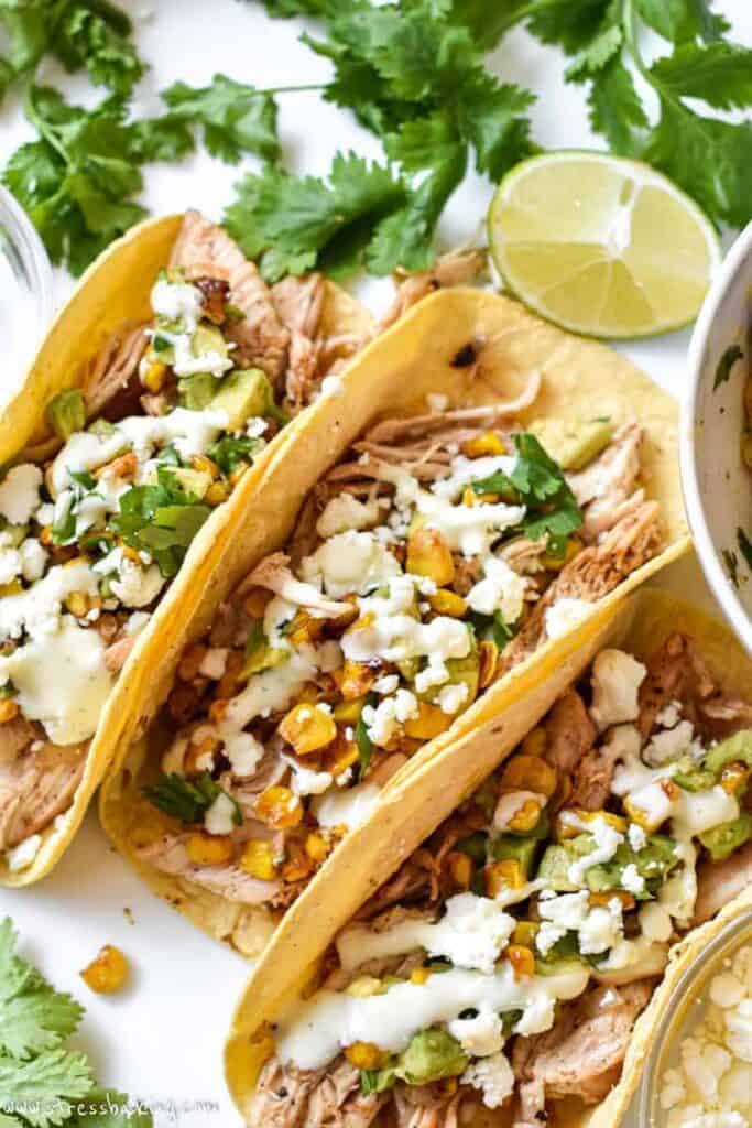 Three mexican street corn tacos on a white platter
