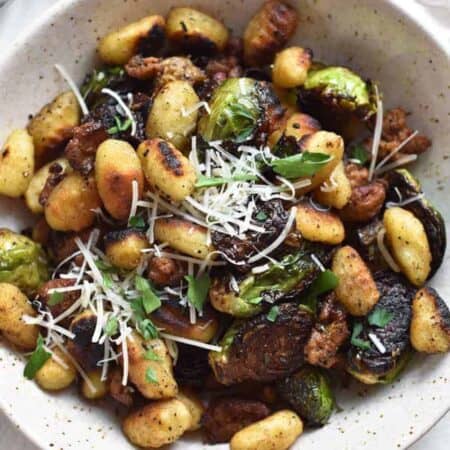 Overhead shot of a speckled bowl of pan fried gnocchi and brussels sprouts topped with shredded cheese