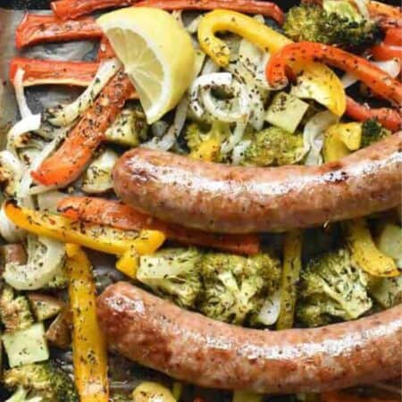 Overhead shot of browned sausages on top of a sheet pan of seasoned roasted veggies