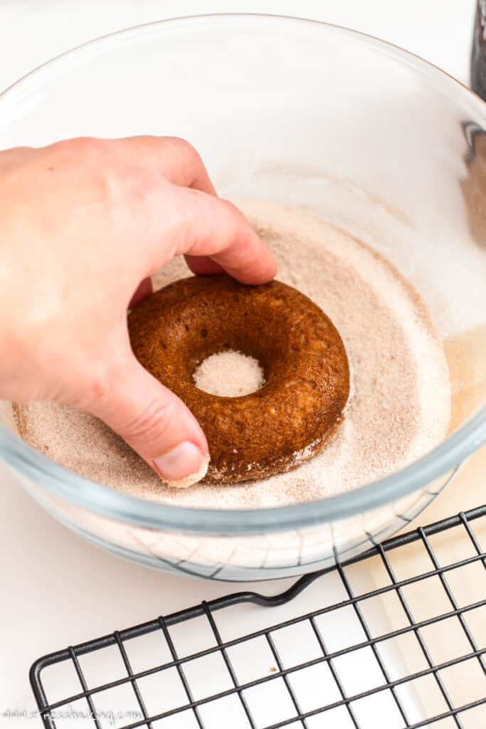 A donut being dipped in cinnamon sugar mixture