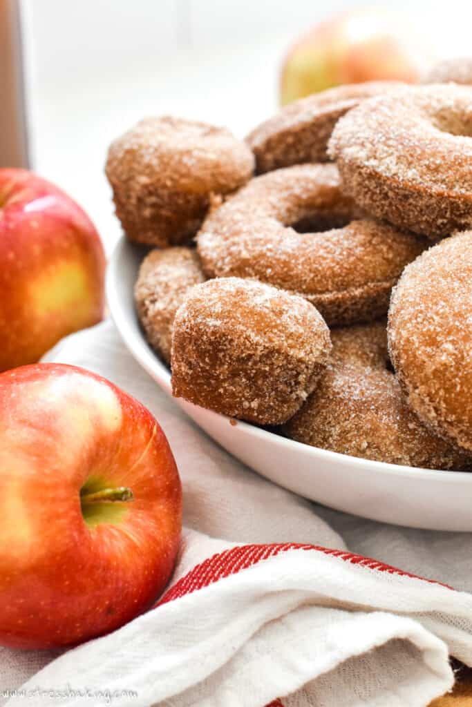 Apple cider donuts and donut holes in a white bowl with red apples